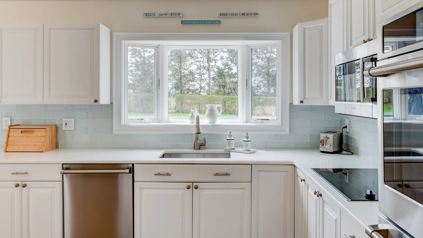Una cocina luminosa con gabinetes blancos, un fregadero y una ventana grande.