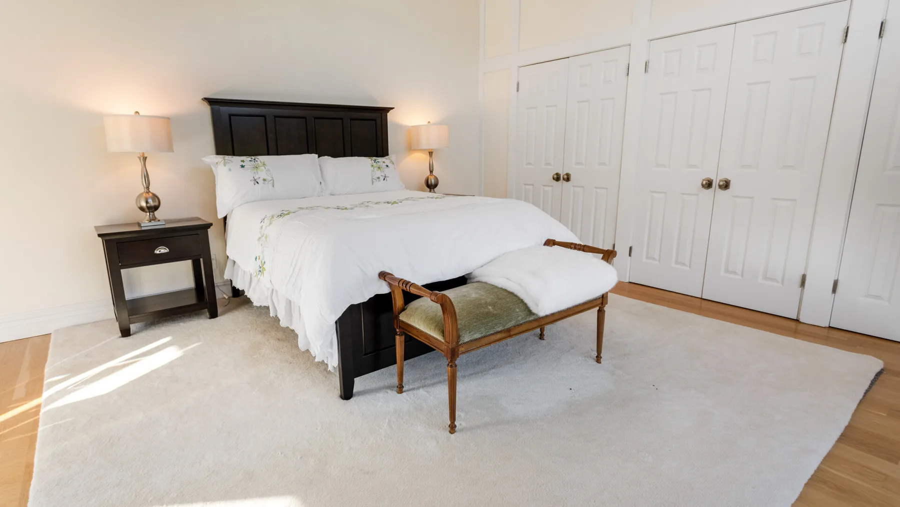 Un dormitorio luminoso con una cama bien tendida y un banco acolchado a sus pies.