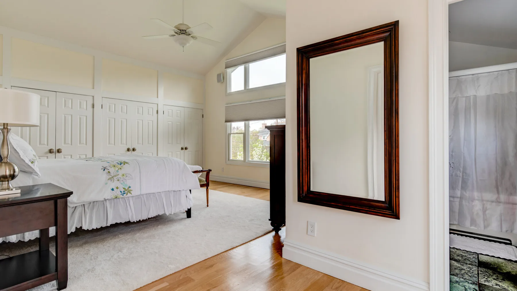 Un dormitorio luminoso con ropa de cama blanca, paredes paneladas y ventanas grandes.