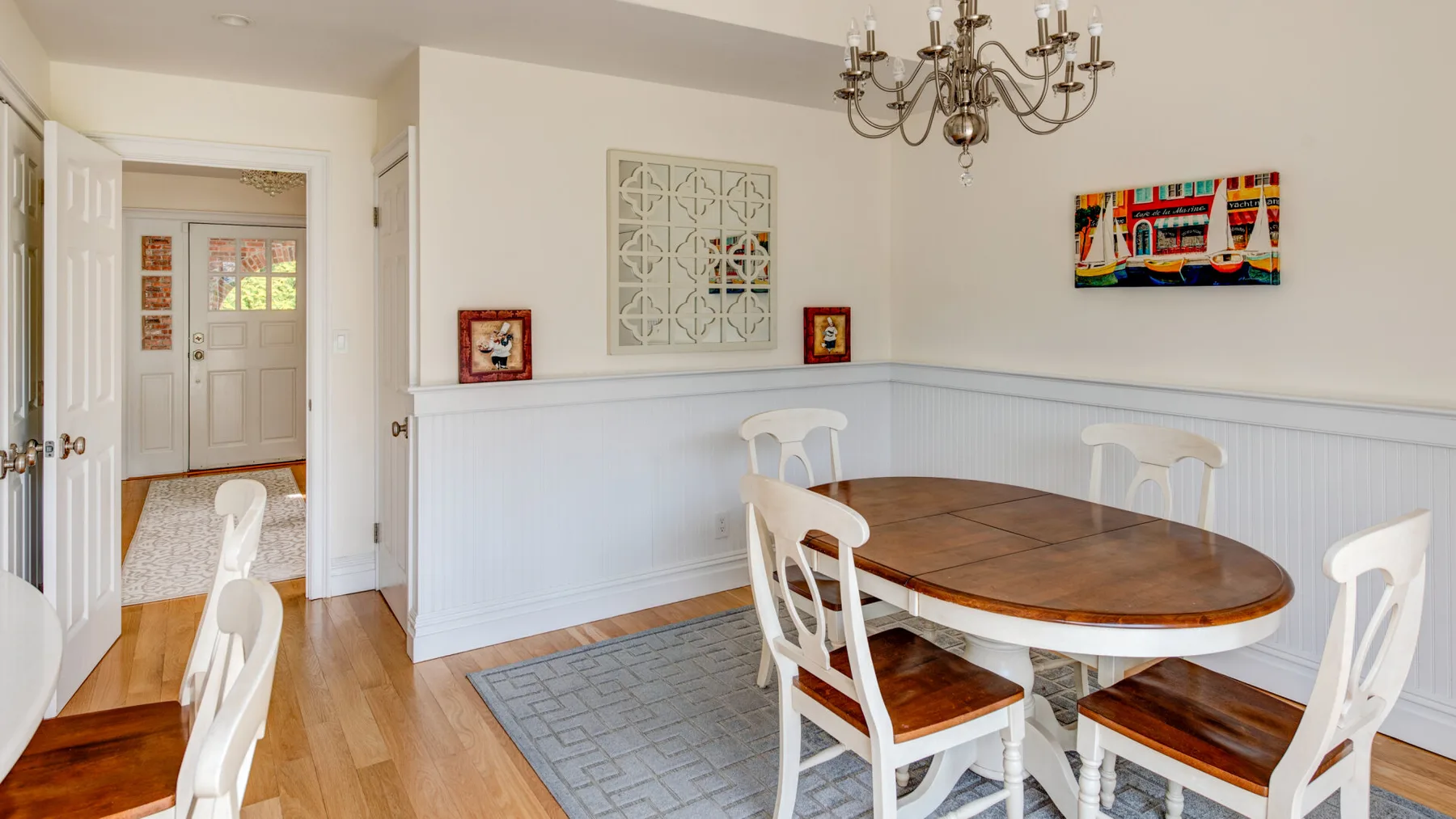 Un comedor con una mesa de madera, sillas blancas y cuadros enmarcados.