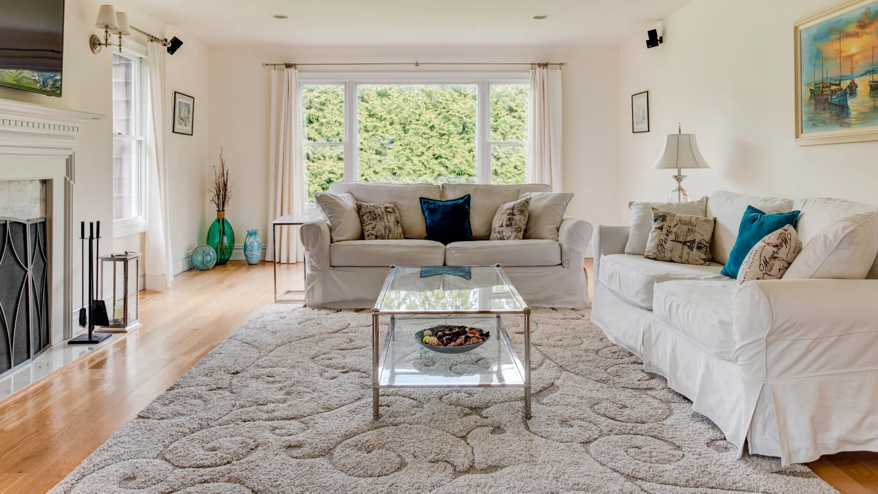 Una sala de estar luminosa con sofás, una mesa de centro de vidrio y grandes ventanas.