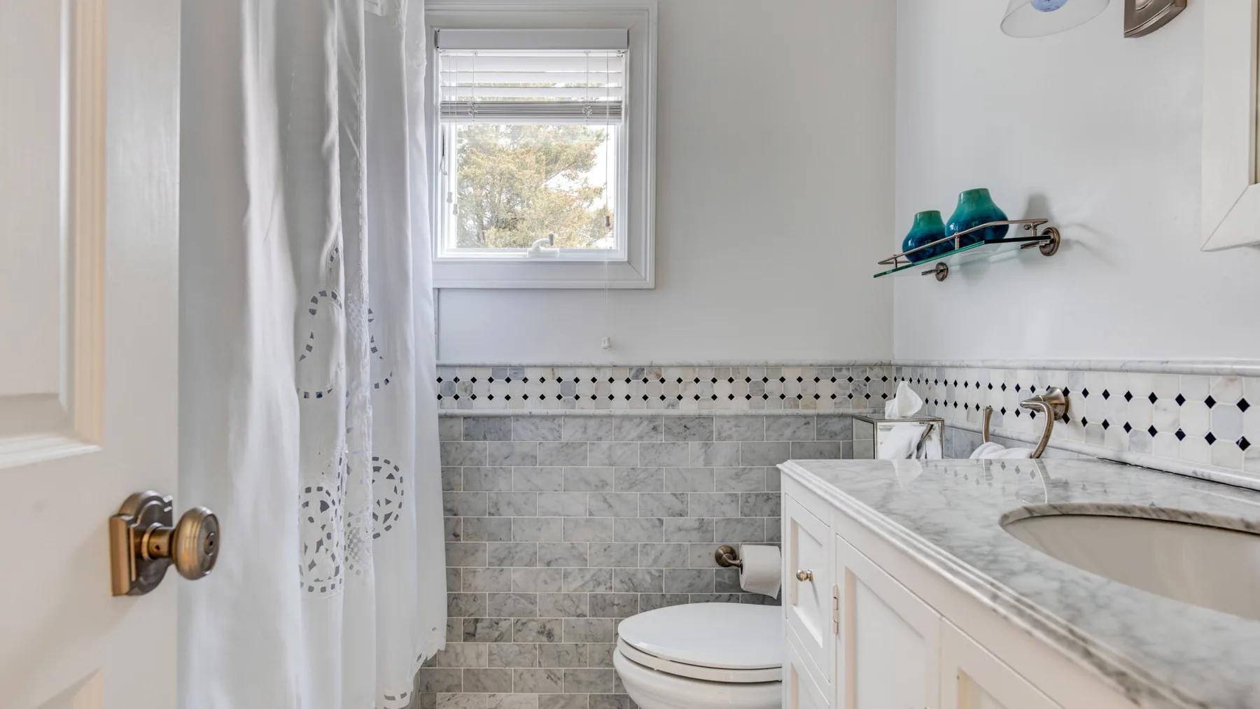 Un baño con bañera, inodoro y una ventana sobre las paredes de azulejos.