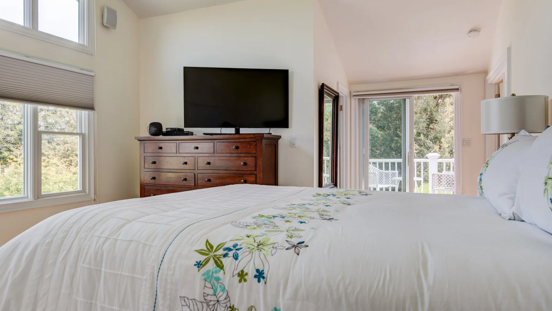 Un dormitorio con cama, televisor y ventanas con vista a un balcón.