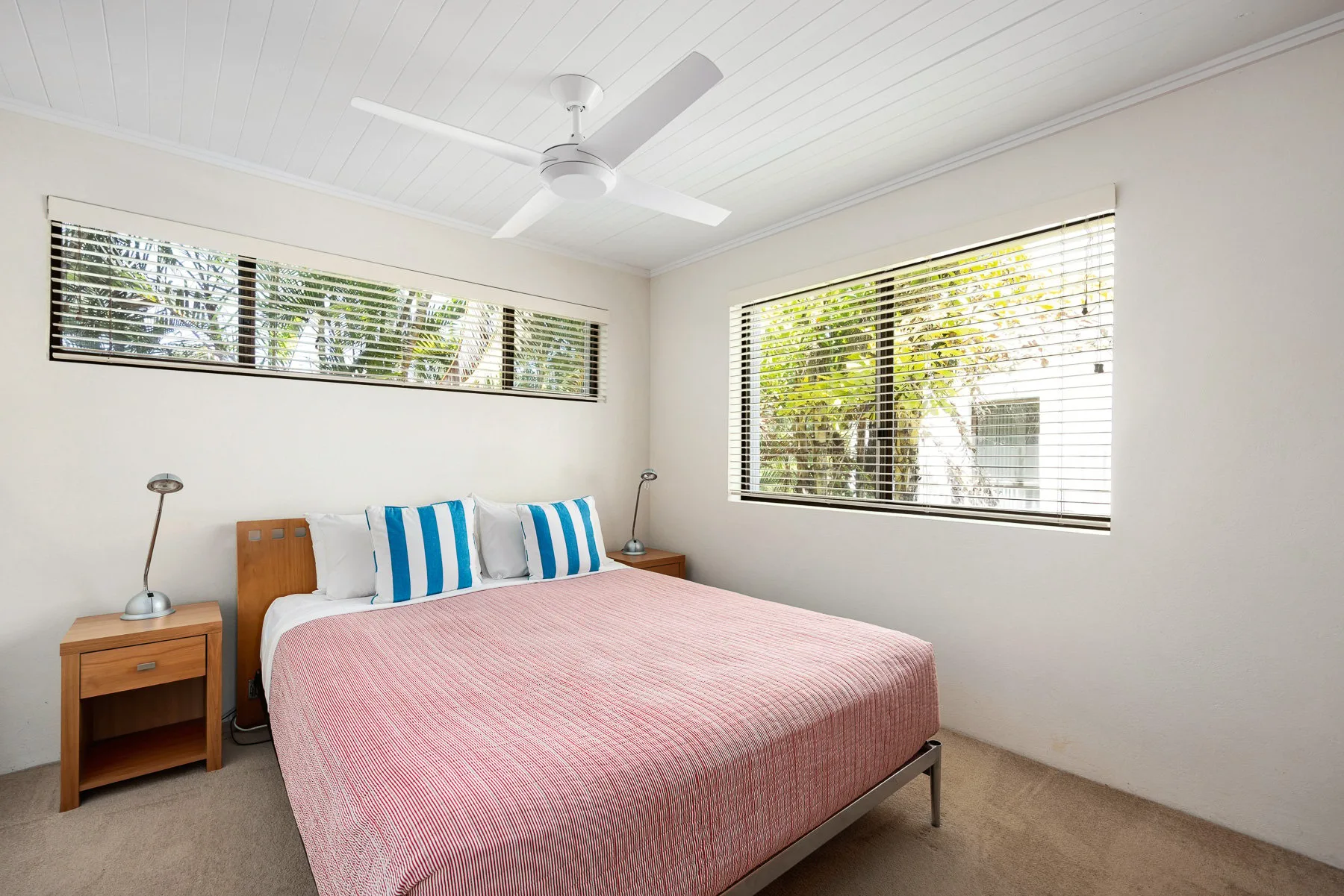 A bedroom with a bed, bedside tables, and windows with blinds.