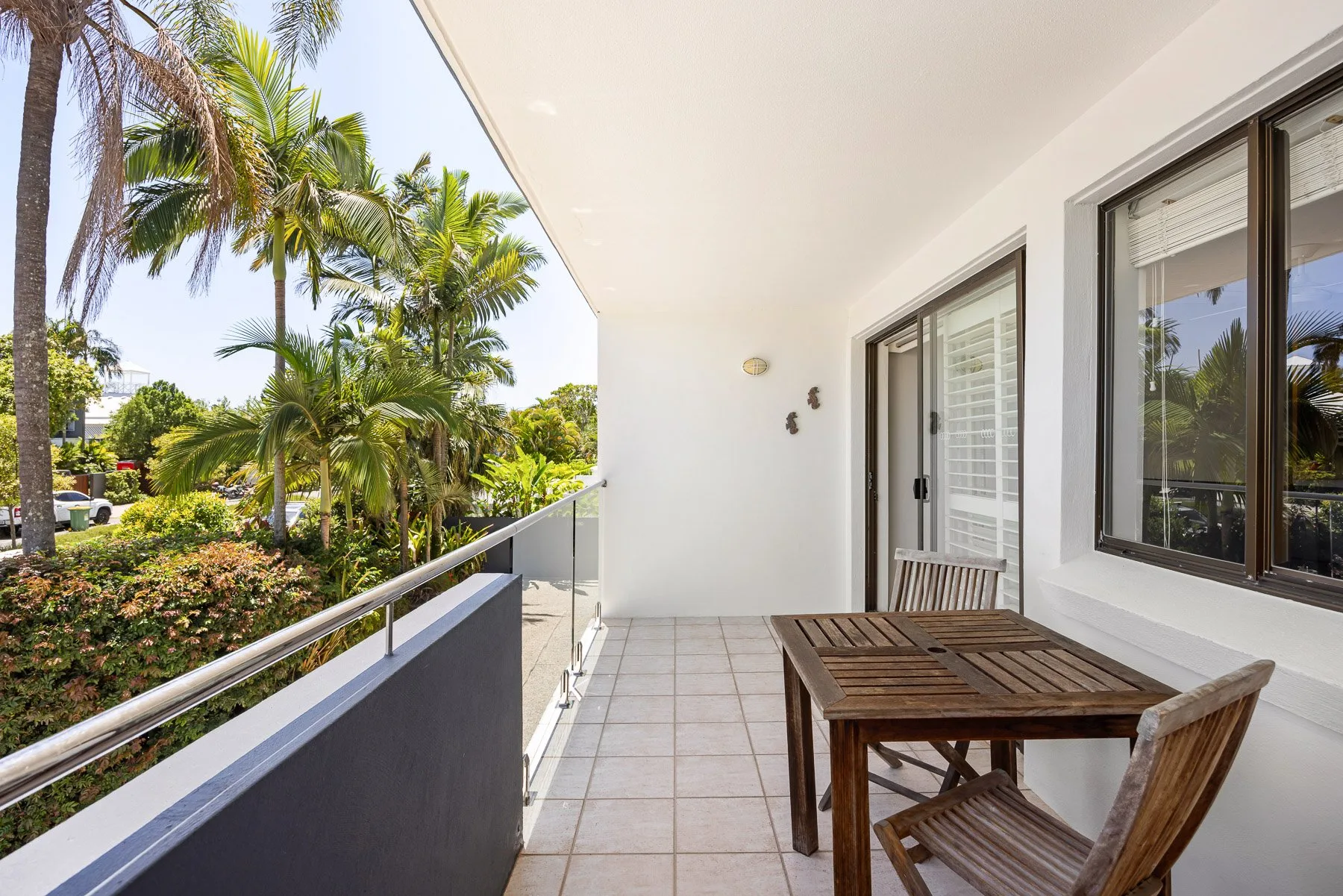 A tiled balcony with wooden seating overlooks palm trees and greenery.