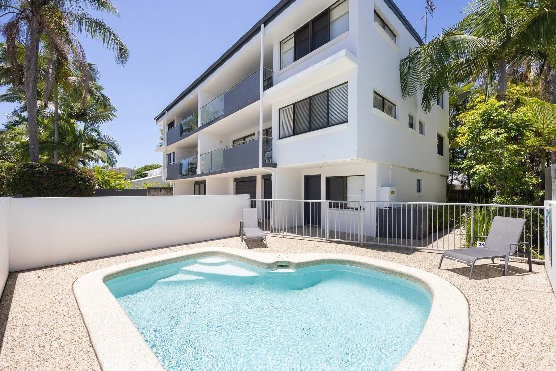 A small outdoor pool sits beside a white multi-story building.