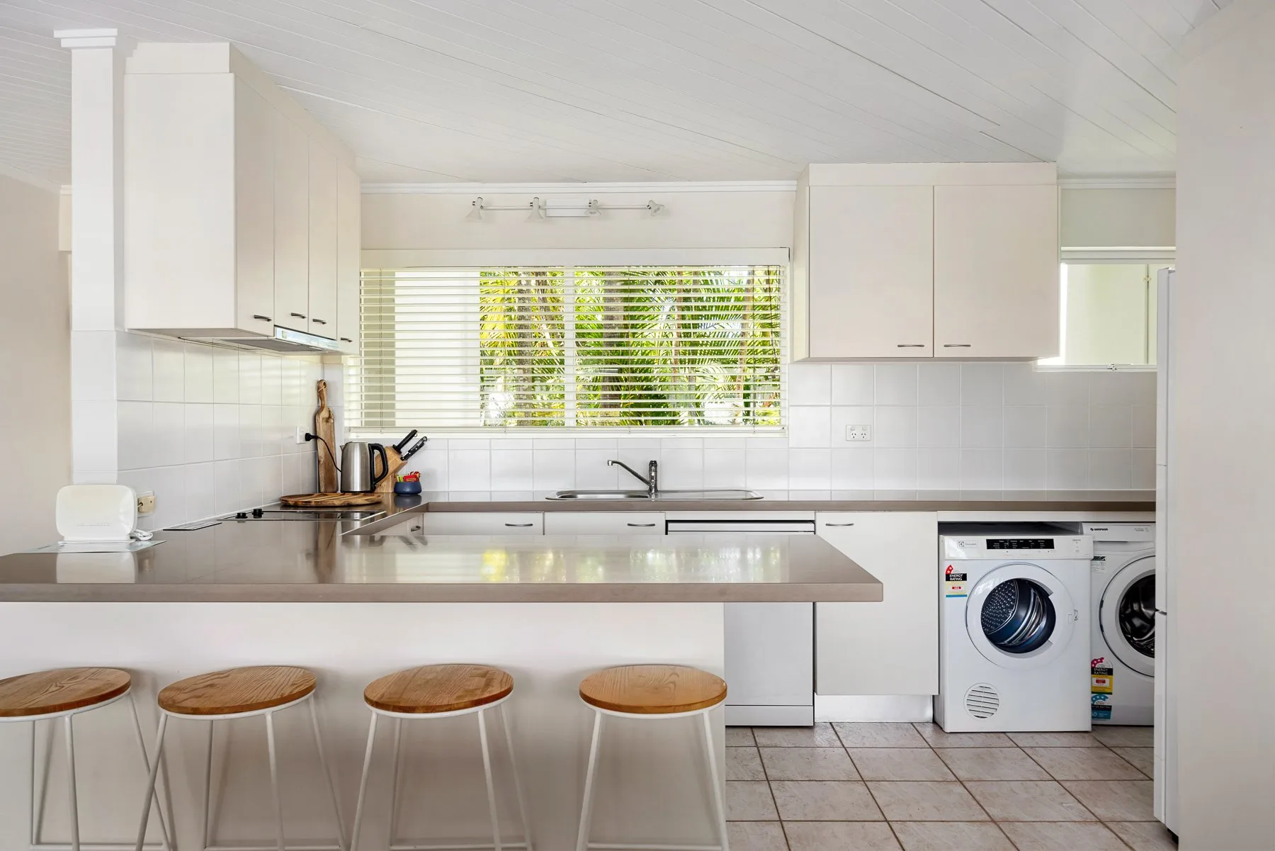 A bright kitchen with a counter, seating, and laundry appliances.
