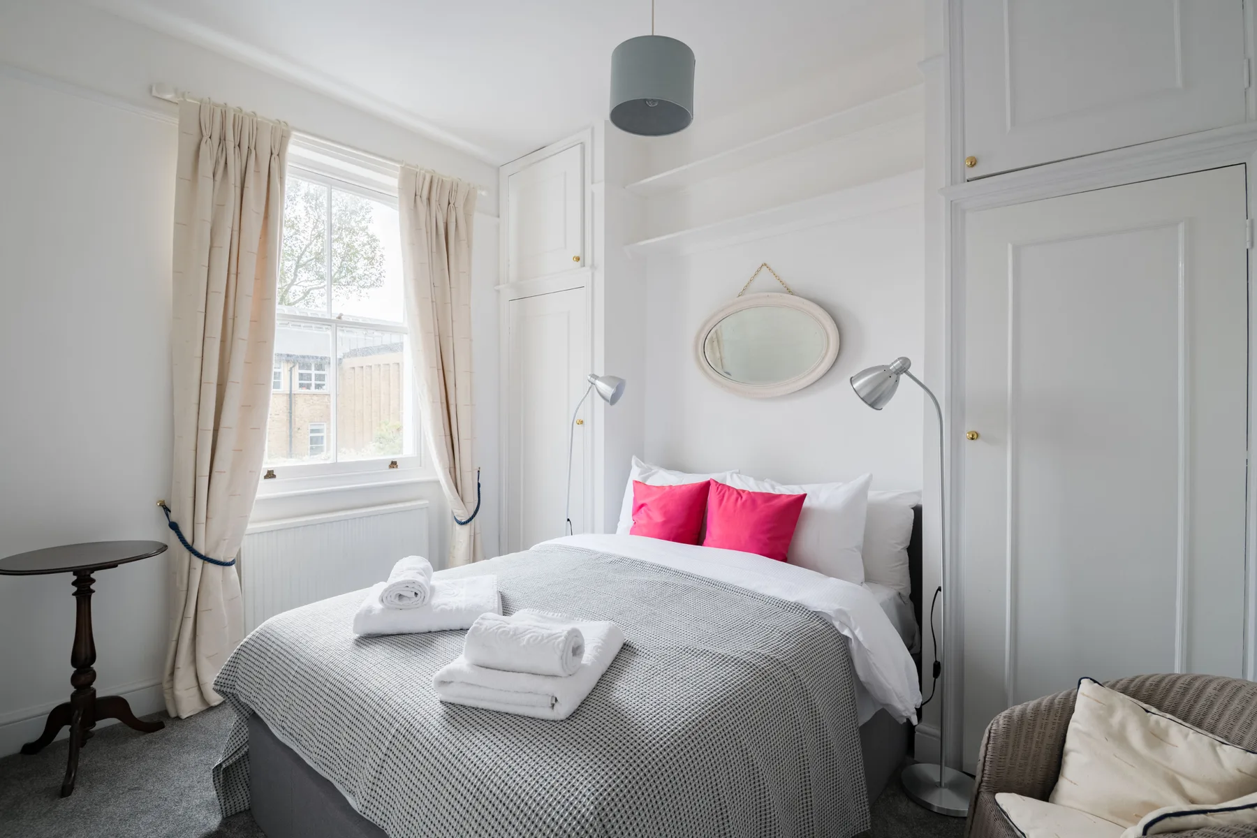 A bright bedroom with a neatly made bed and a window framed by curtains.