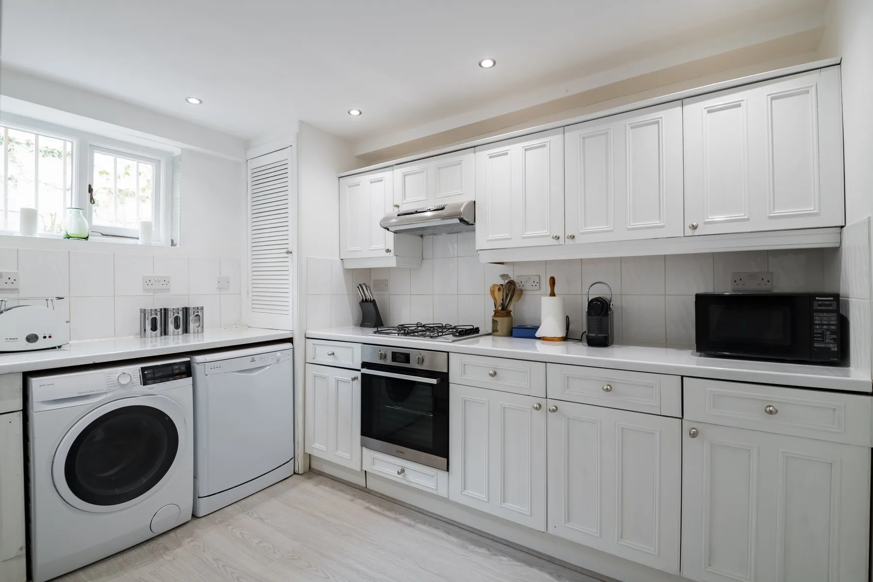 A bright white kitchen with built-in cabinetry, a stove, and laundry appliances.