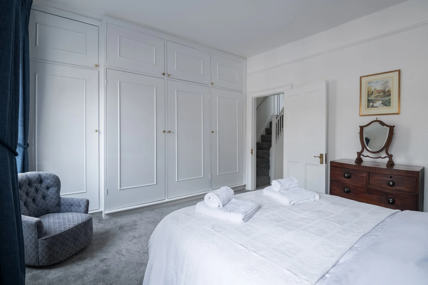 A bedroom with a neatly made bed and built-in wardrobes along the wall.