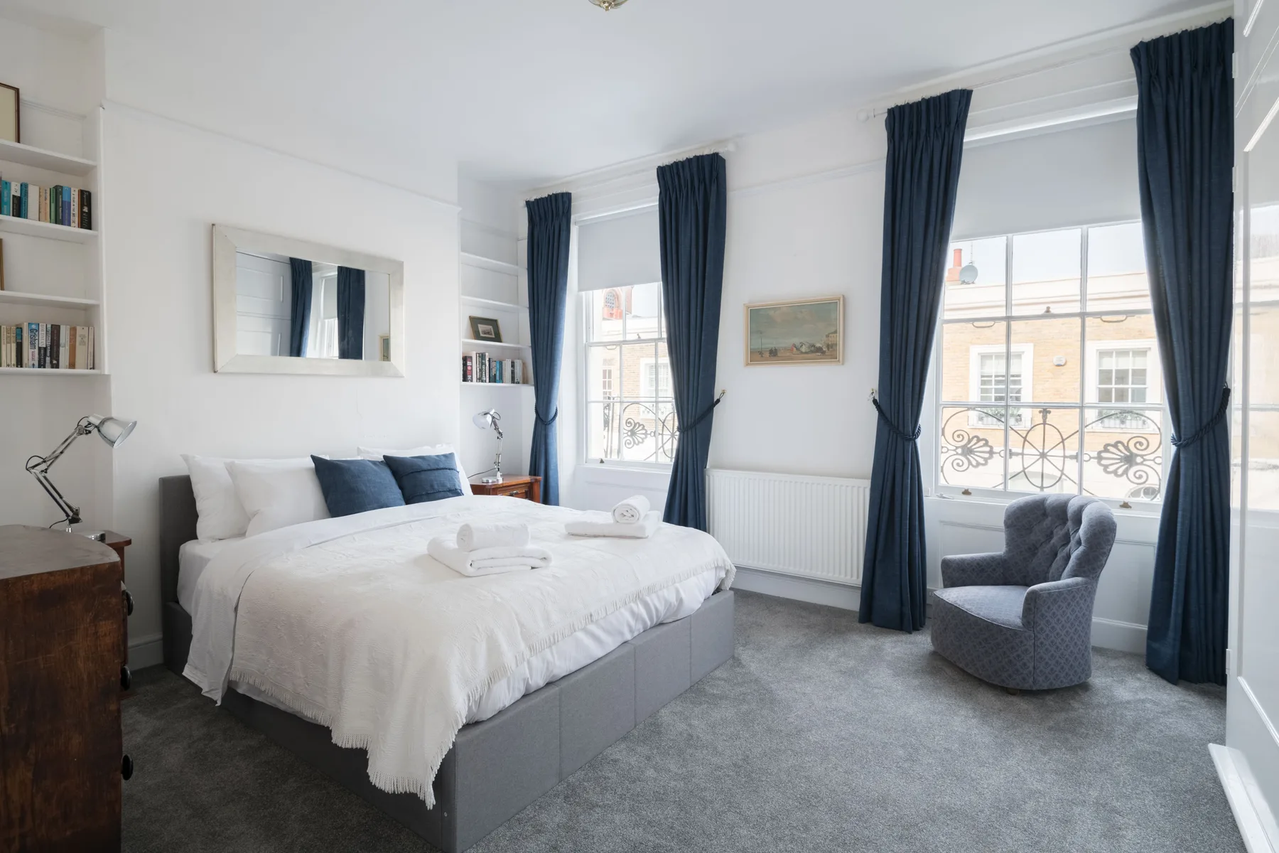 A bright bedroom with a neatly made bed and tall windows dressed with dark curtains.
