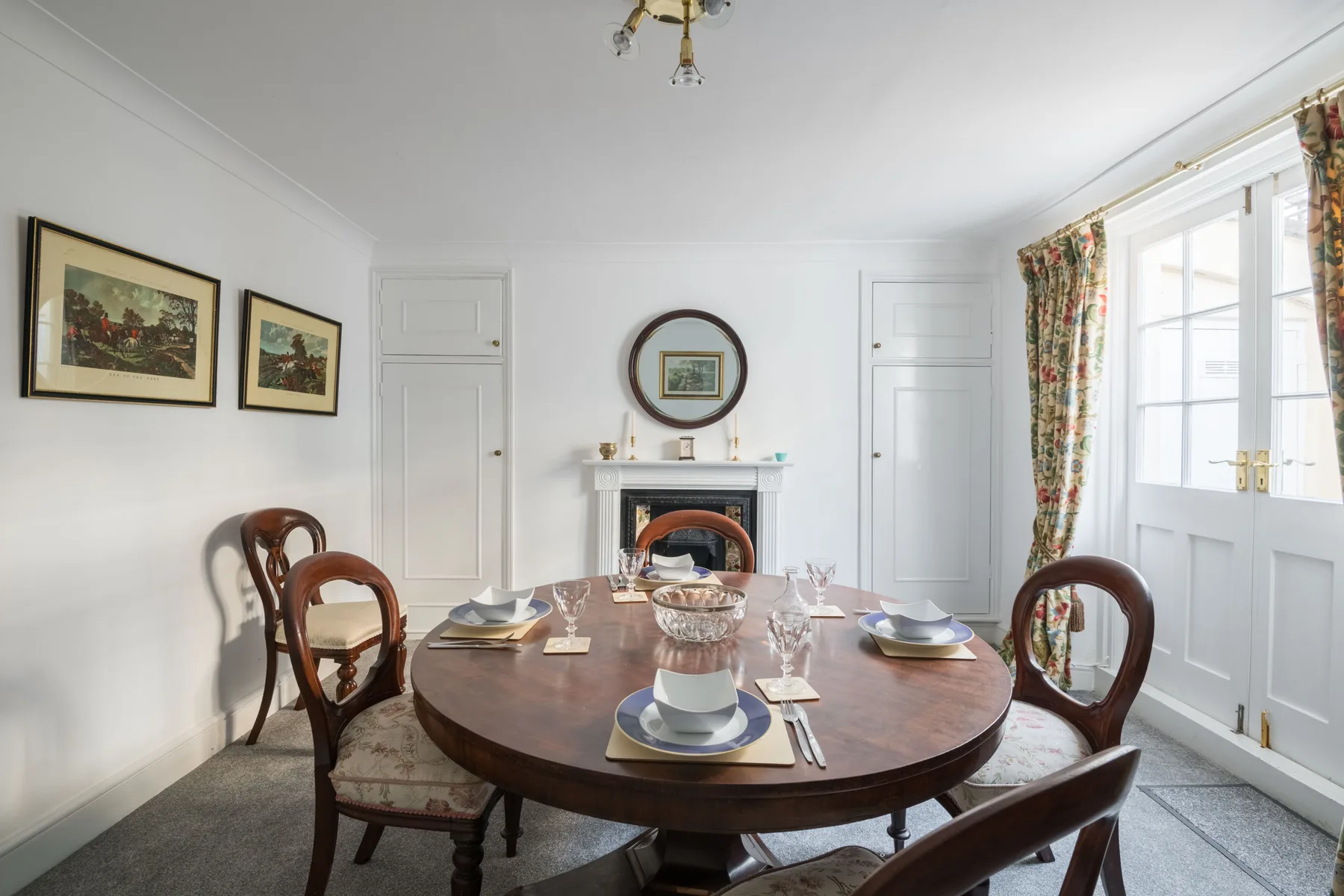 A bright dining room with a round wooden table and large windows.