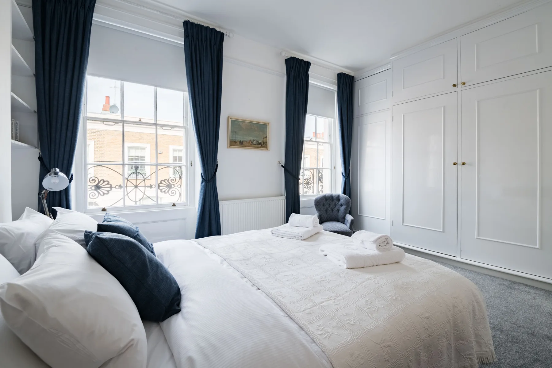 A bright bedroom with a large bed, tall windows, and dark curtains.