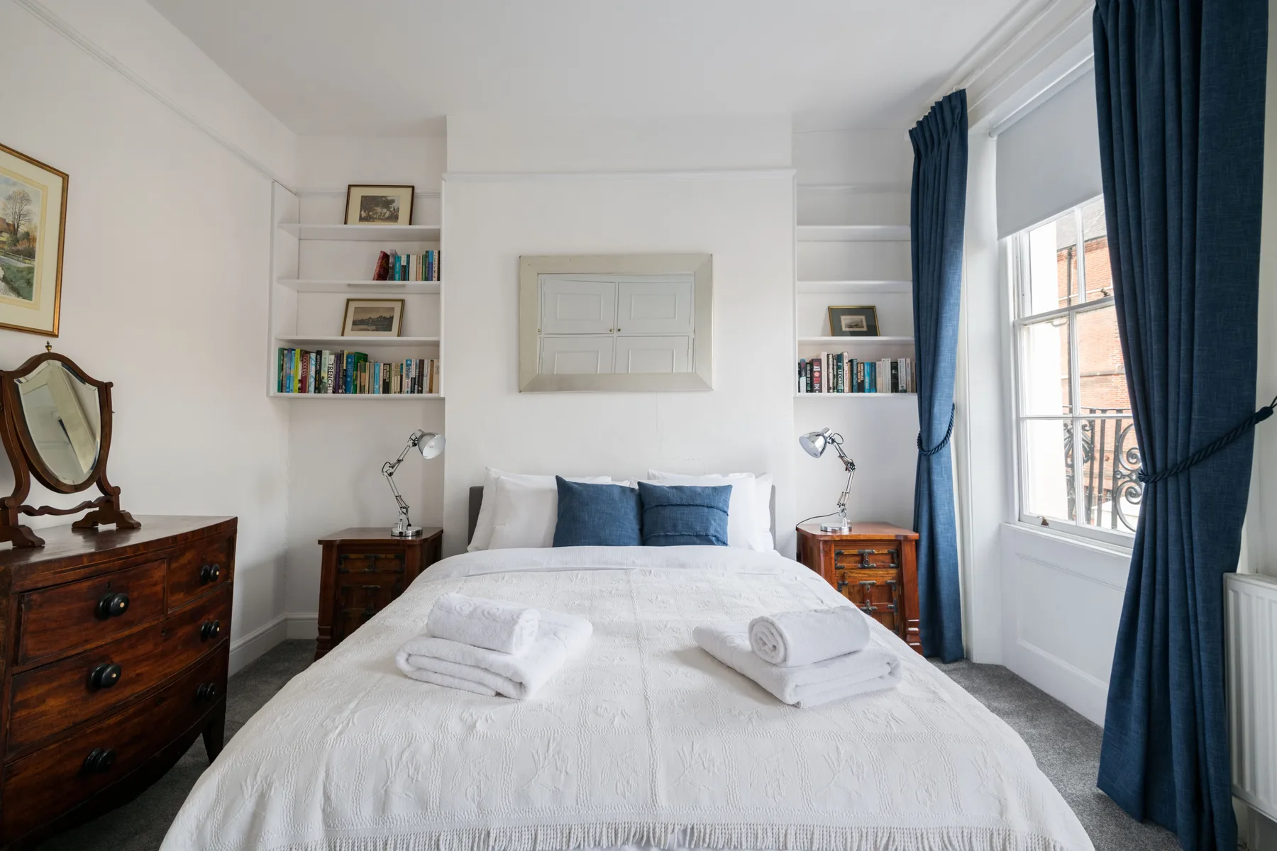 A bright bedroom with a neatly made bed and blue curtains by the window.