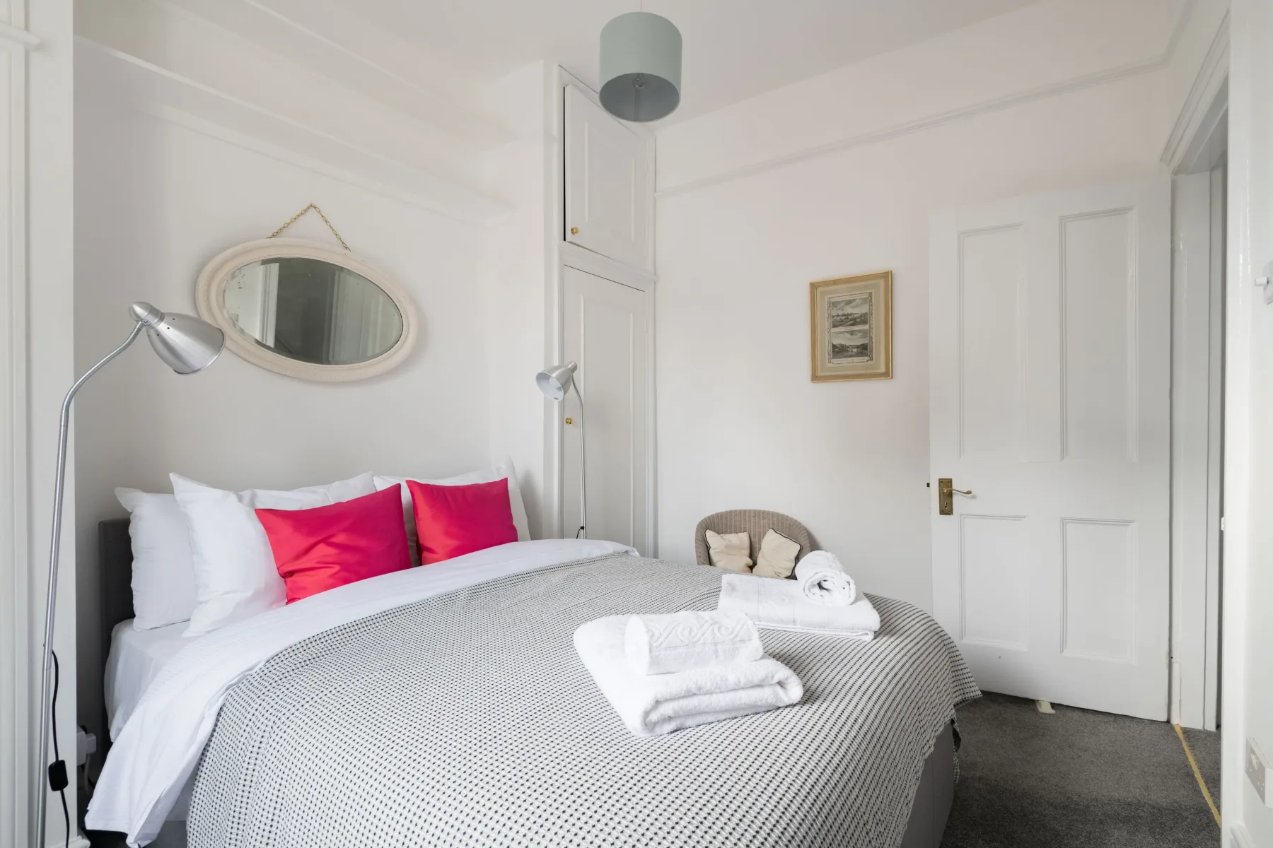 A bedroom with a neatly made bed, bright accent pillows, and an oval wall mirror.