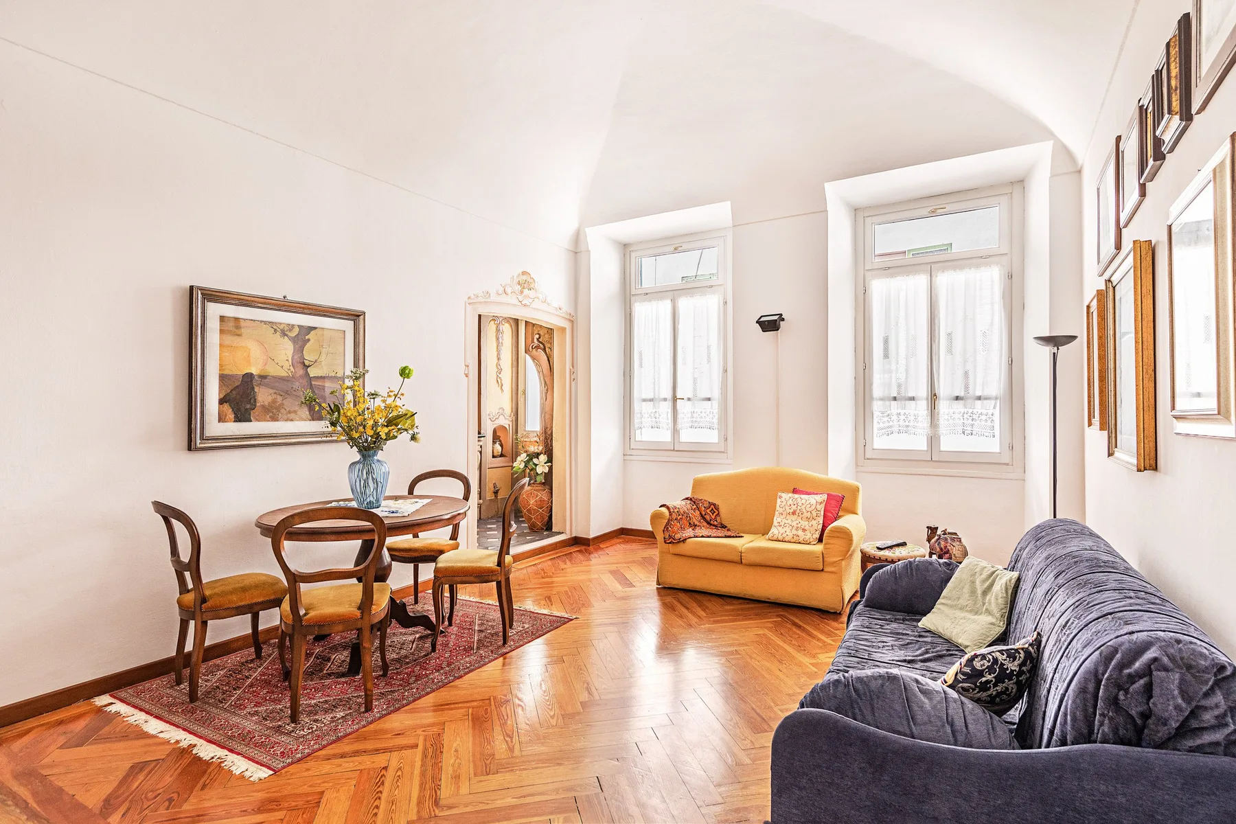 Sala de estar luminosa con asientos, una mesa de comedor y ventanas altas.