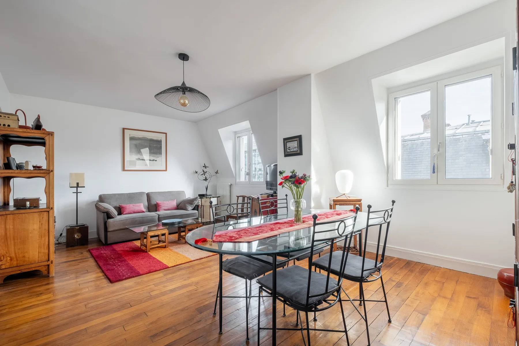 Zona de comedor y sala con una mesa de vidrio, asientos y ventanas grandes.
