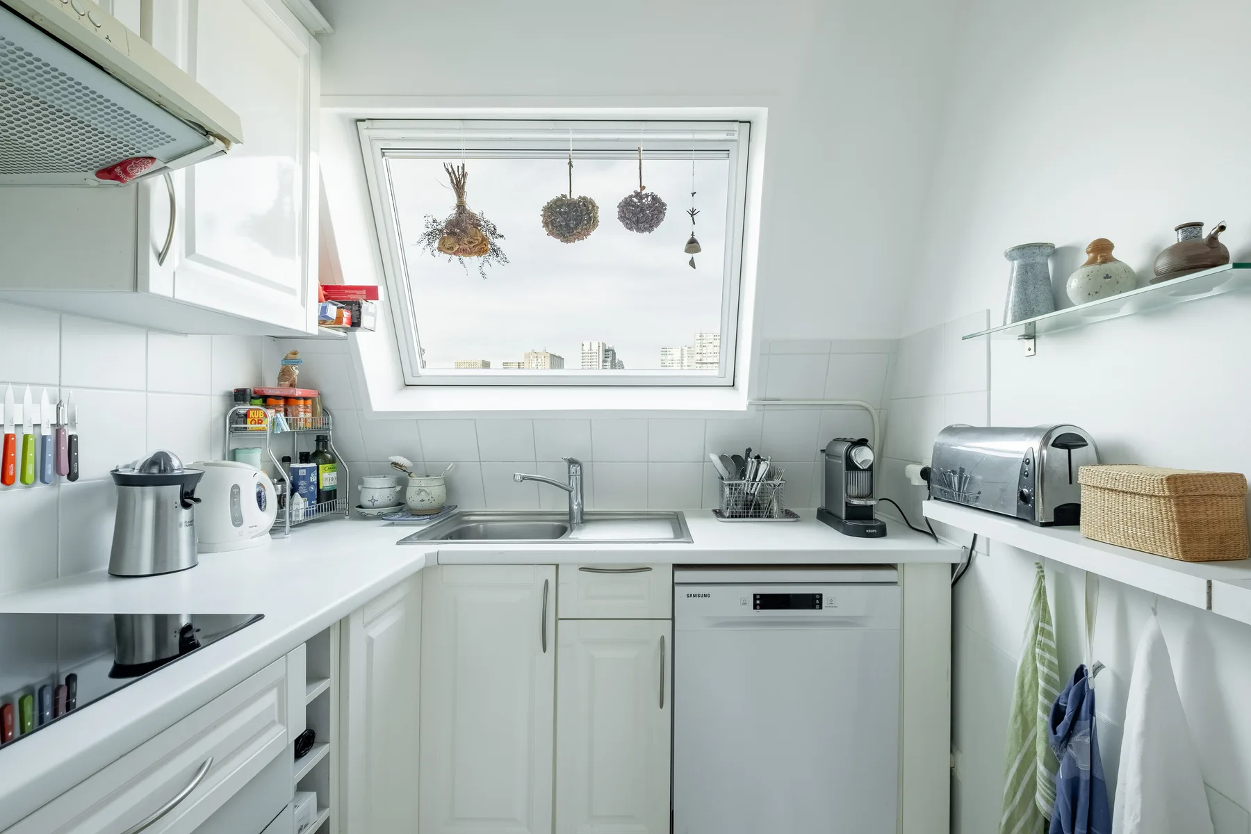 Una cocina blanca y luminosa con encimeras, un fregadero y pequeños electrodomésticos.