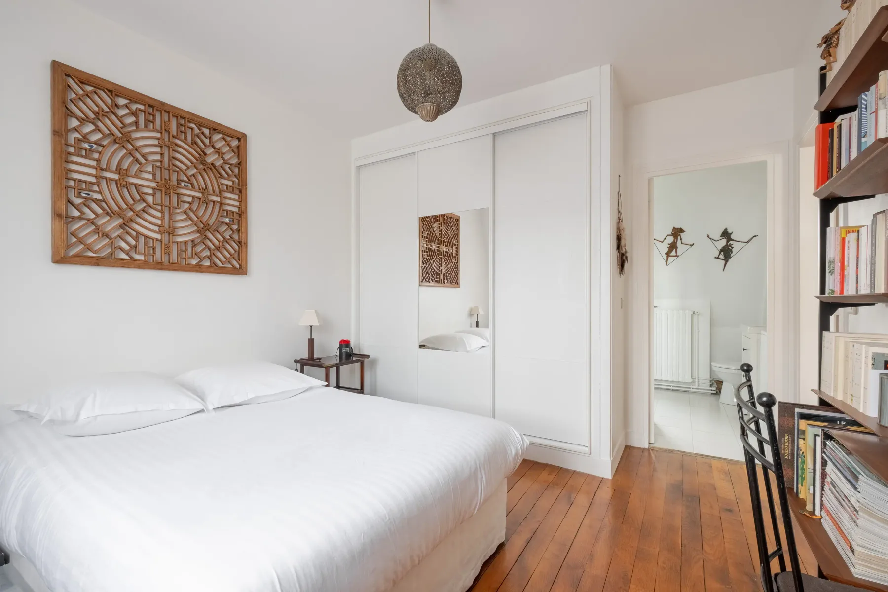 Un dormitorio luminoso con una cama blanca, un armario empotrado y estanterías.