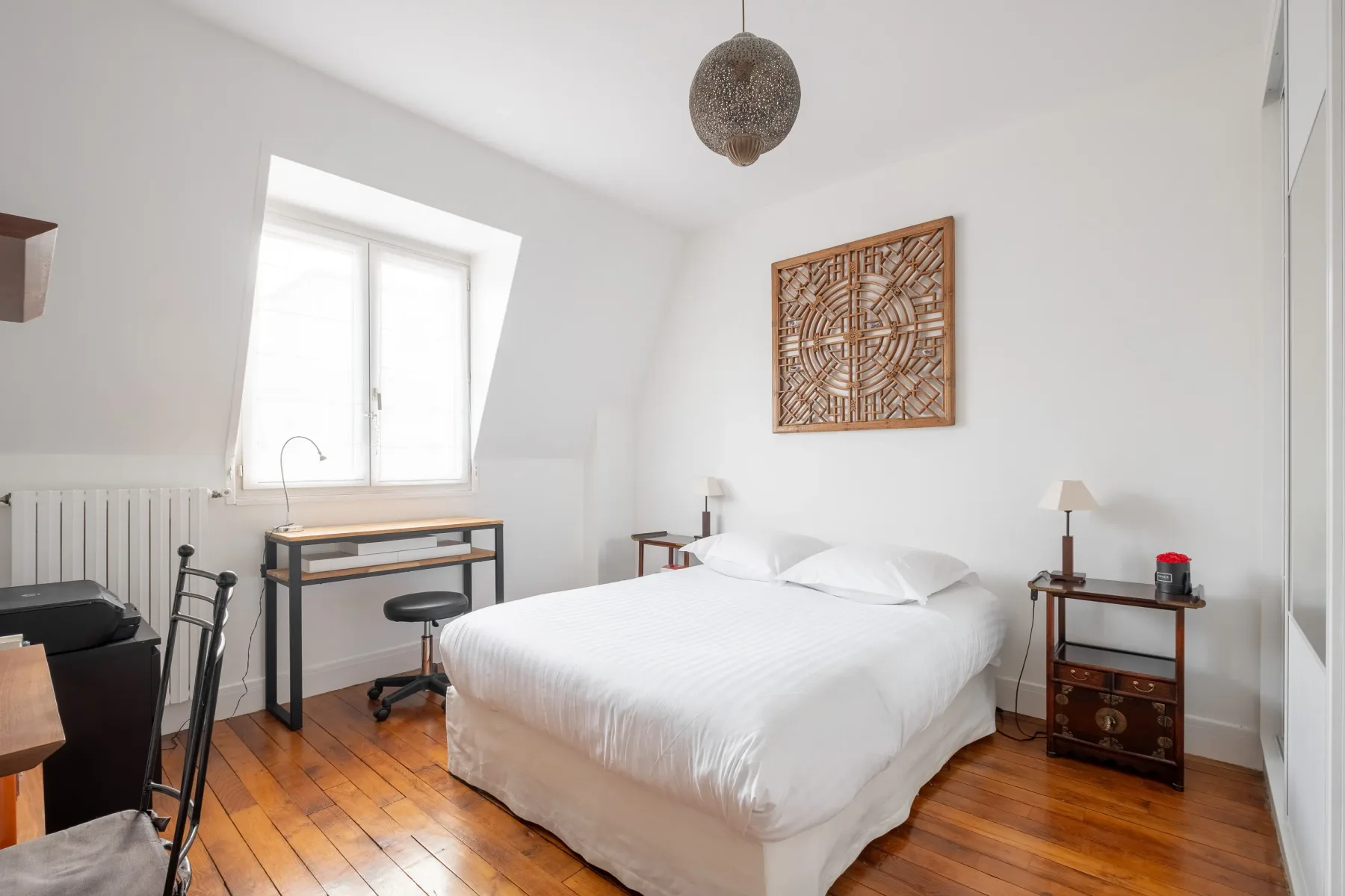 Un dormitorio luminoso con una cama blanca, suelo de madera y arte en la pared.