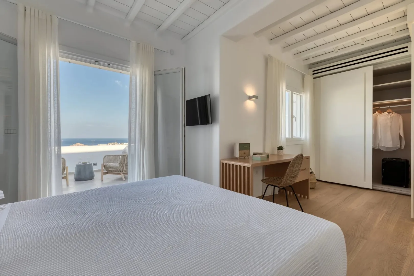 A bedroom with a desk beside an open wardrobe.