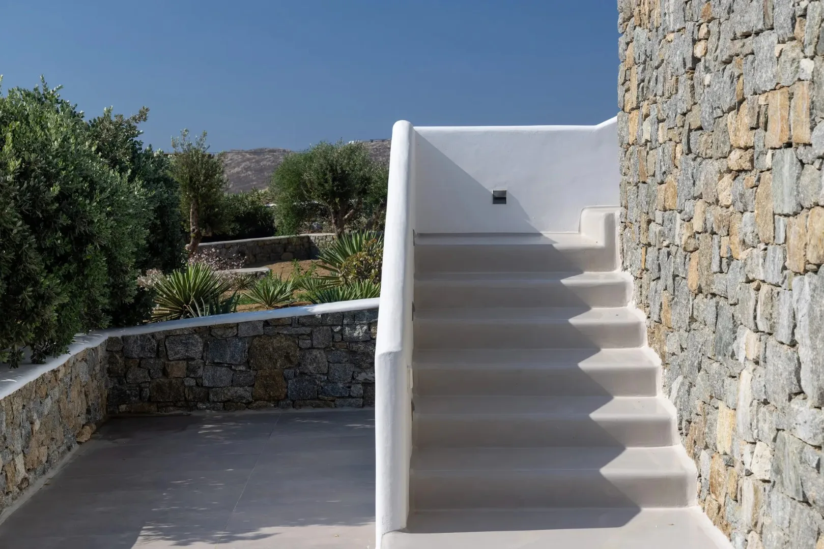 An outdoor stairway with white steps beside a stone wall.