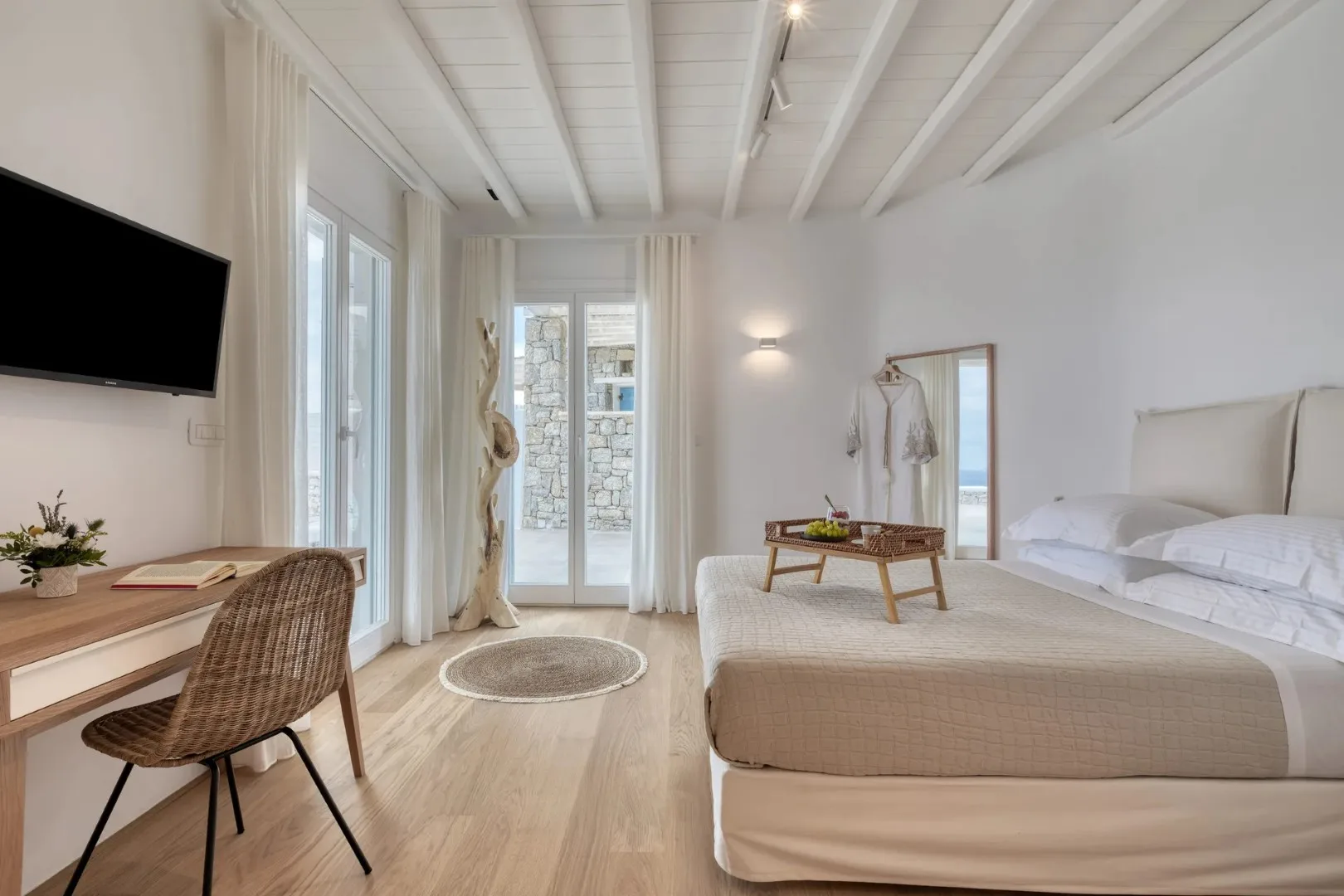 A bright bedroom with a bed, desk, and tall glass doors.