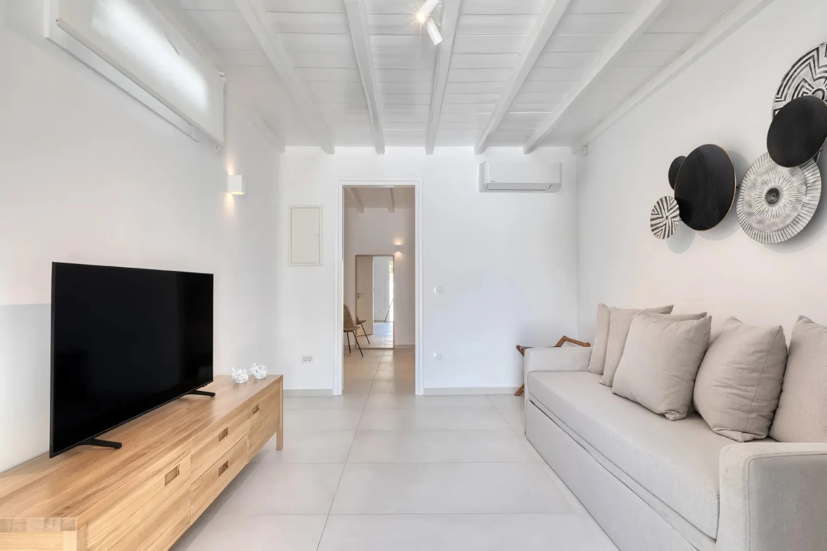 Una sala luminosa con un televisor y asientos de color claro.