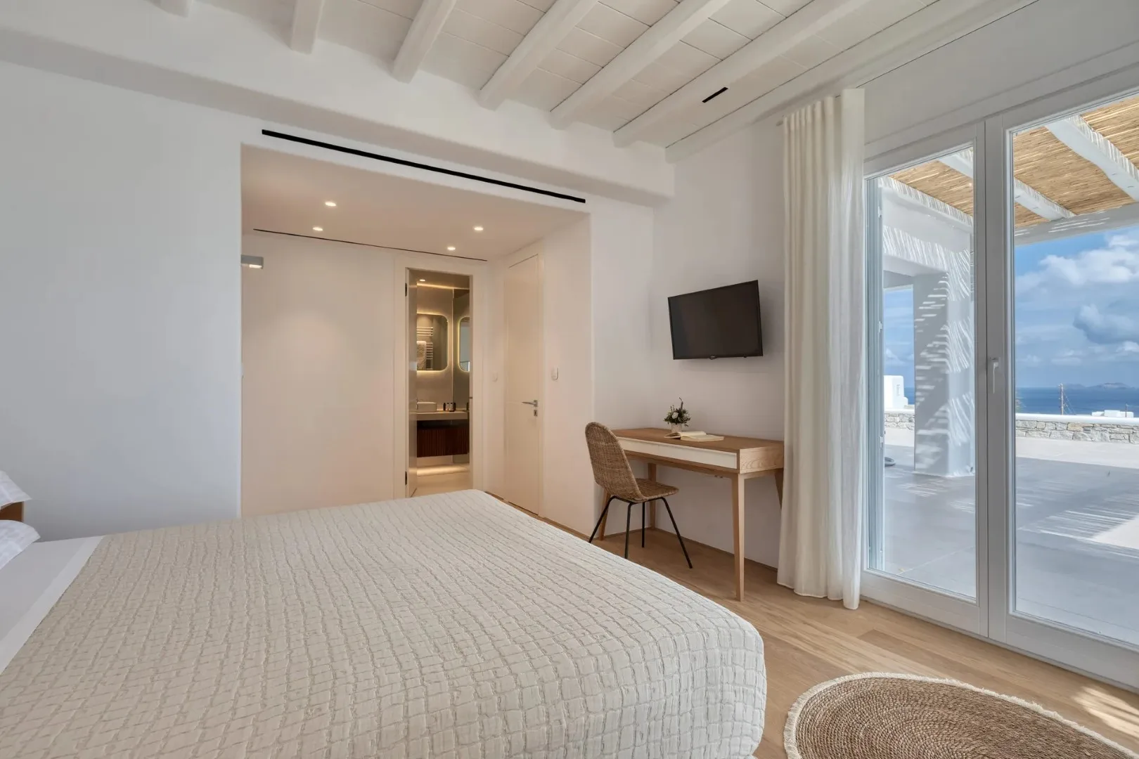 A bright bedroom with a bed, desk, and sliding glass doors to a balcony.