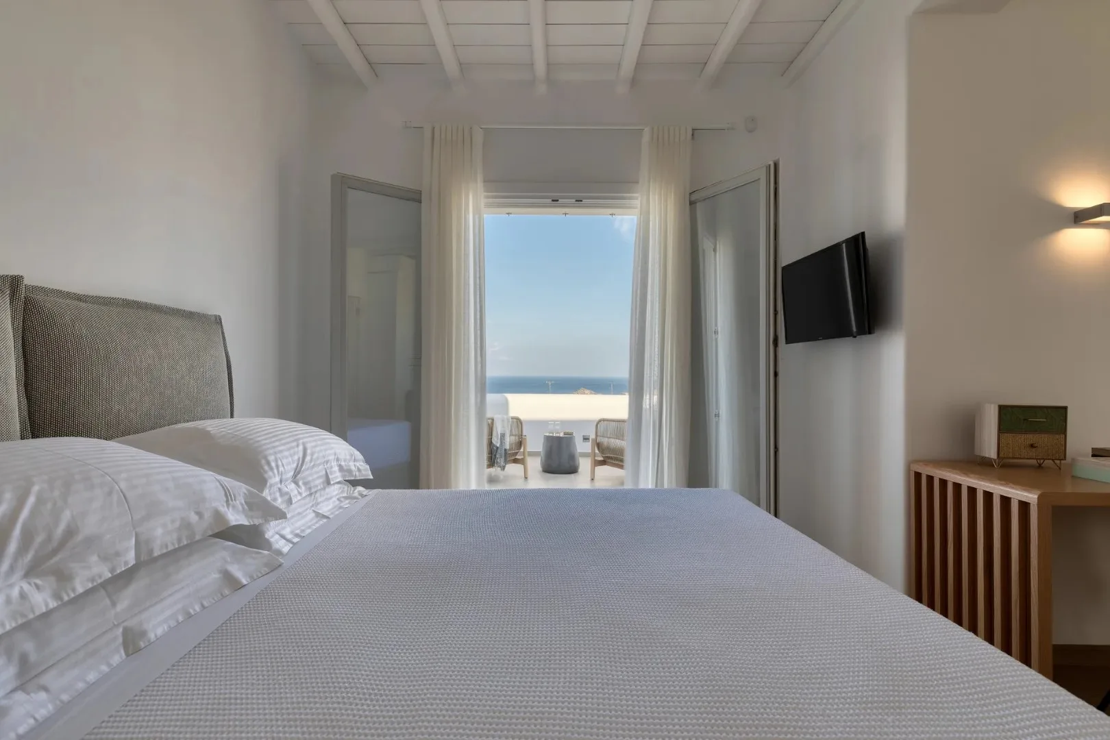 A bedroom with a bed facing open doors to a sea view.