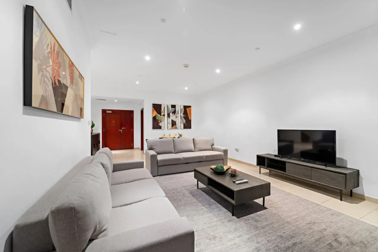 Una sala luminosa con asientos grises, una mesa de centro y un televisor.