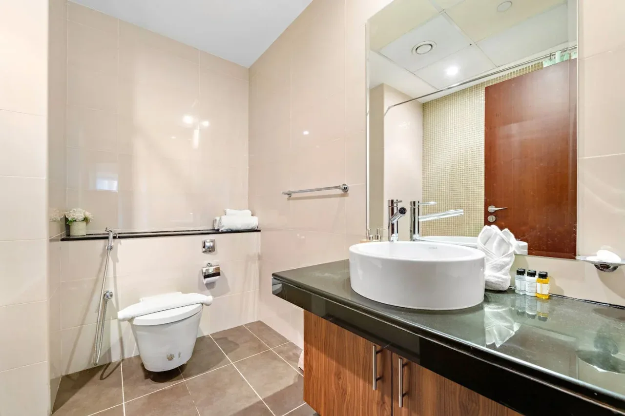 Un baño alicatado con inodoro, lavabo y un gran espejo de pared.