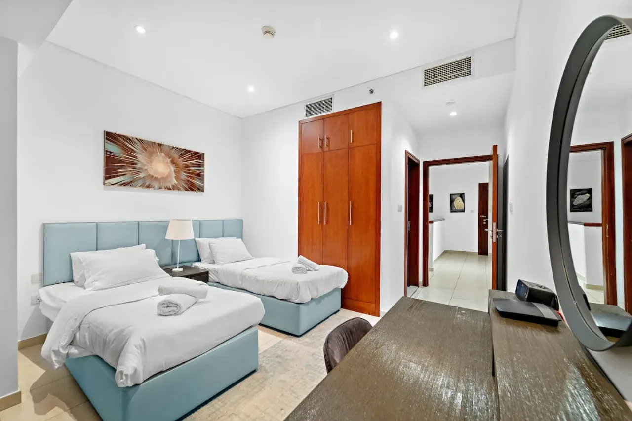 Un dormitorio luminoso con dos camas, un armario de madera y arte en la pared.