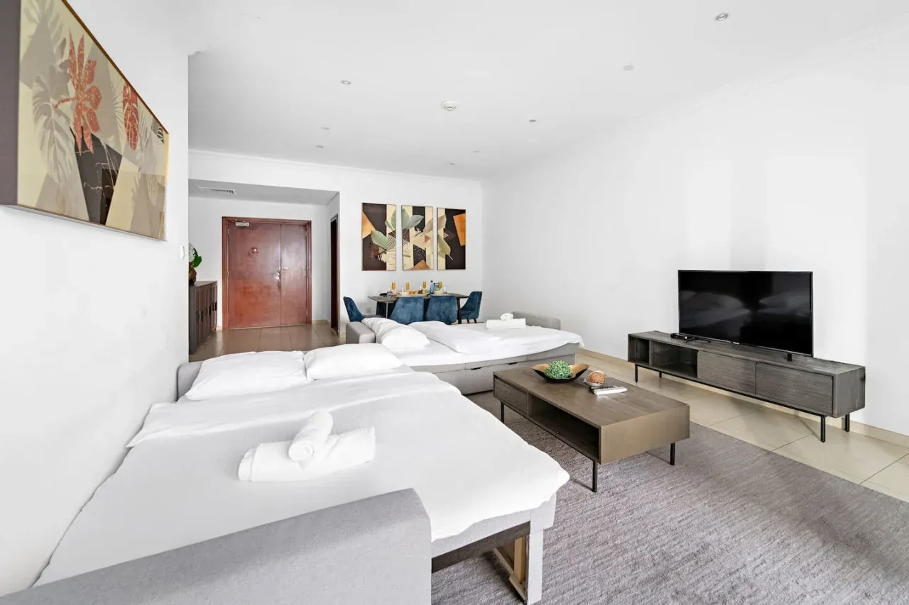 Una sala luminosa con asientos blancos, una mesa de centro y un televisor.