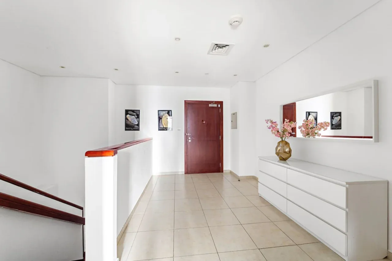 Un pasillo interior luminoso con suelo de baldosas, cuadros y un arreglo floral.