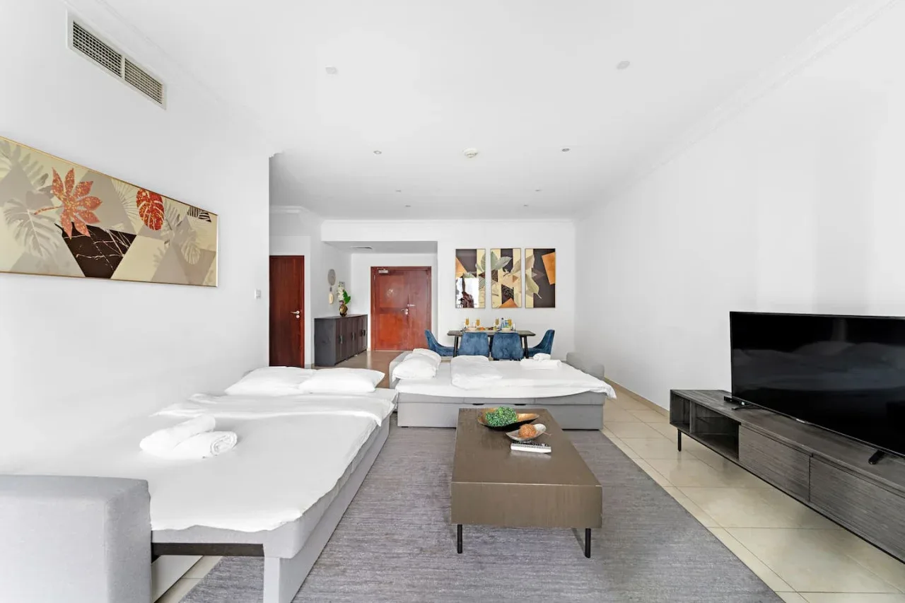 Una sala luminosa con asientos blancos, una mesa de centro y un televisor.