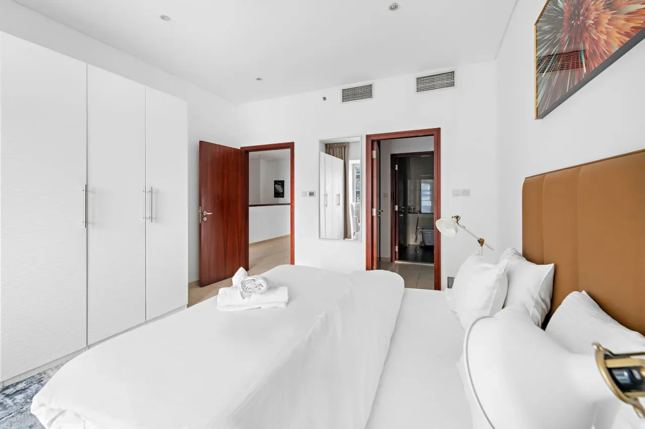 Un dormitorio luminoso con una cama grande, ropa de cama blanca y armarios empotrados.