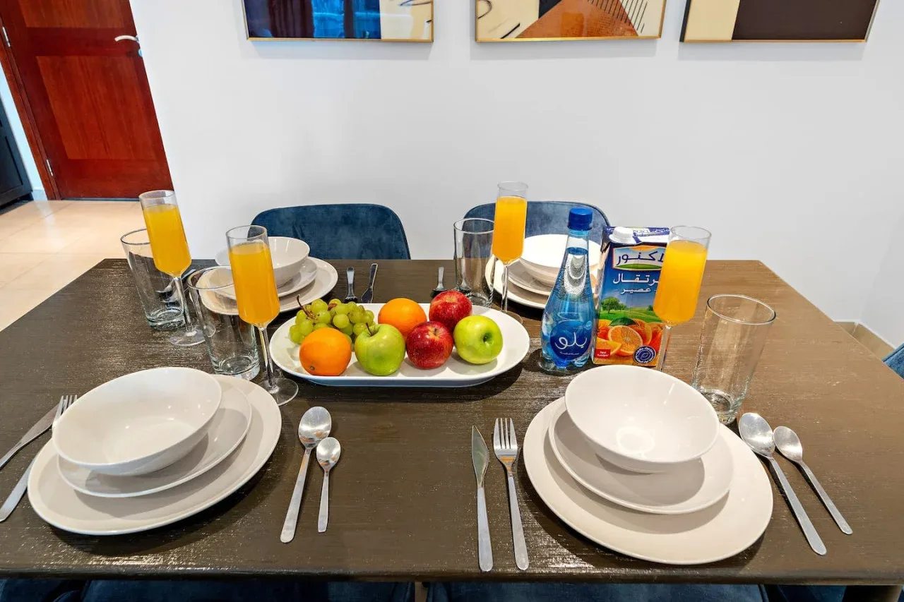 Una mesa de comedor está preparada con platos, fruta, zumo y agua.