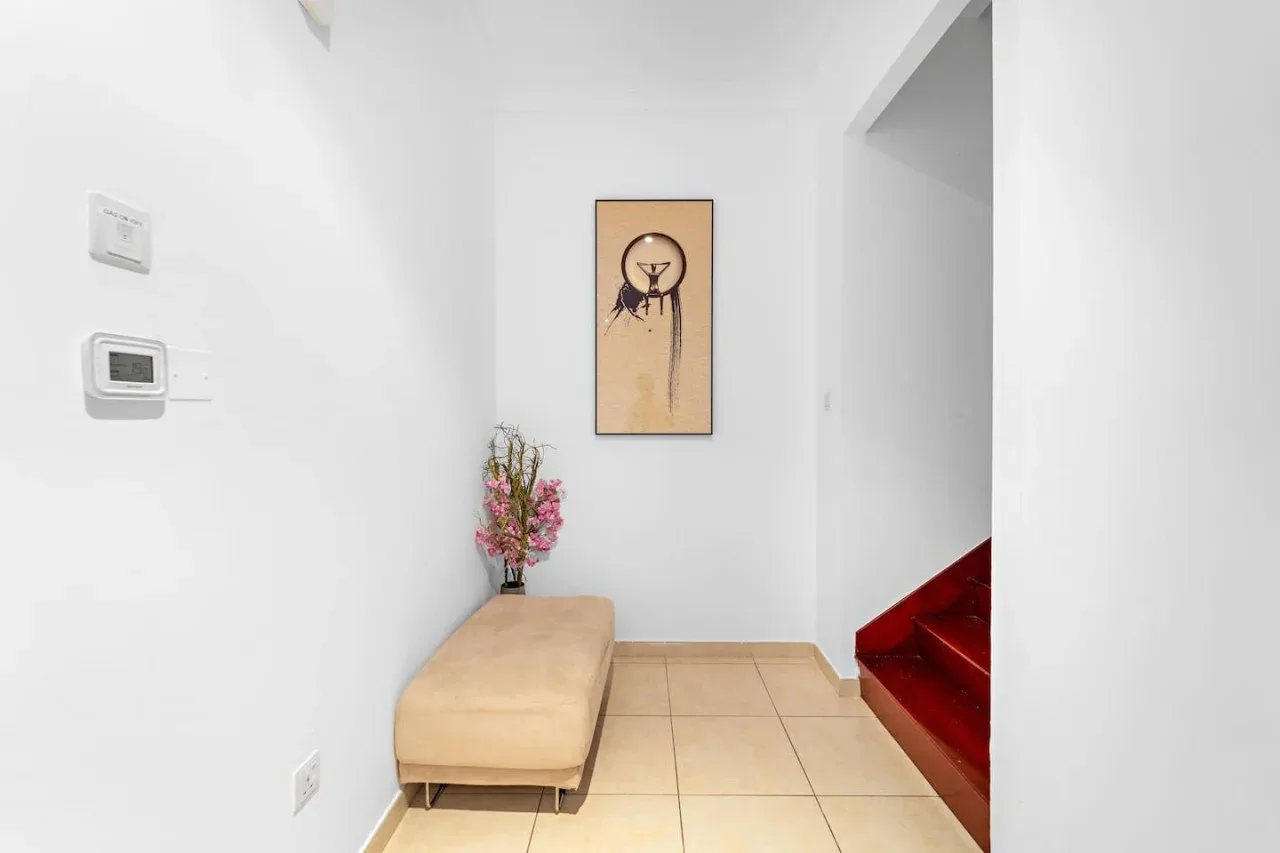 Un pasillo luminoso con un banco acolchado, arte en la pared y escaleras rojas.