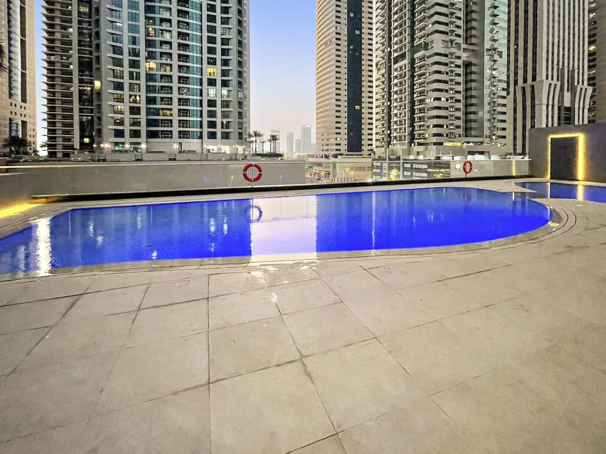 Una piscina exterior está junto a una terraza pavimentada y edificios altos.