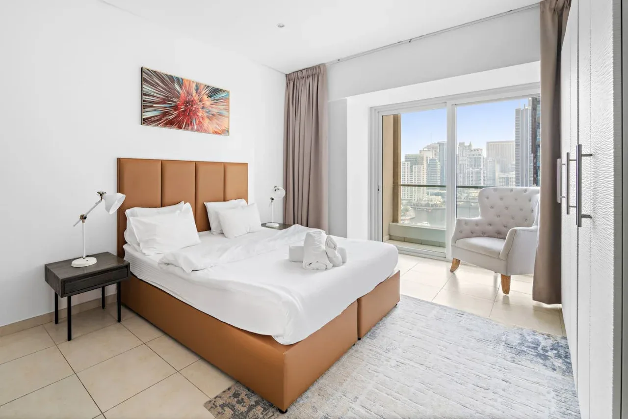 Un dormitorio luminoso con una cama bien hecha y una ventana amplia con vistas a la ciudad.