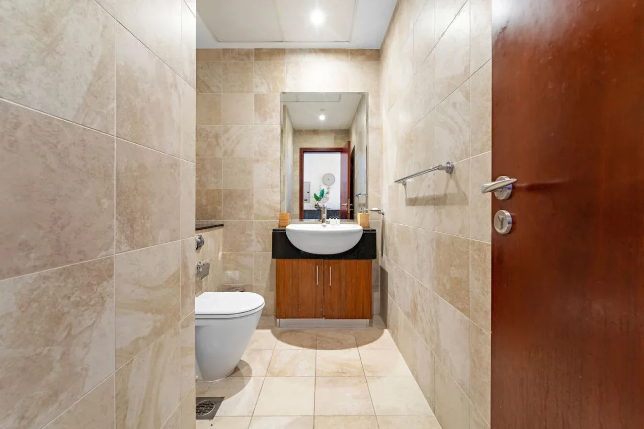 Un baño revestido de azulejos con inodoro, lavabo y un espejo grande.