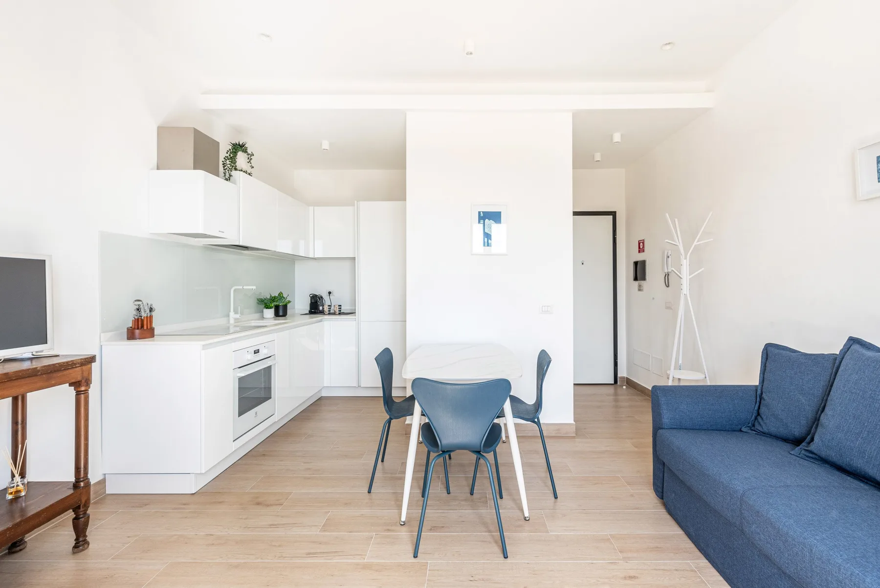 Una sala luminosa y diáfana combina una cocina blanca, una mesa de comedor y asientos azules.
