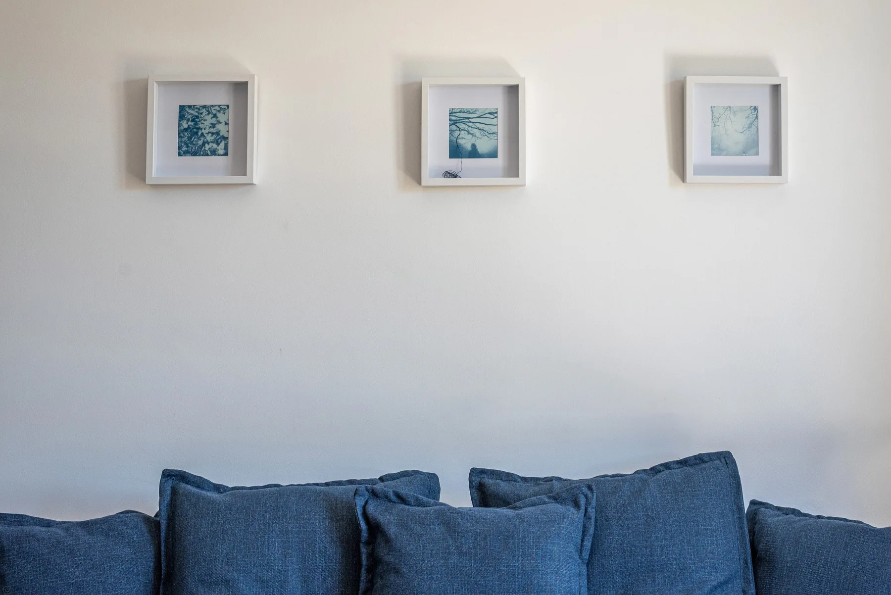 Una pared de sala de estar con tres cuadros sobre asientos azules.
