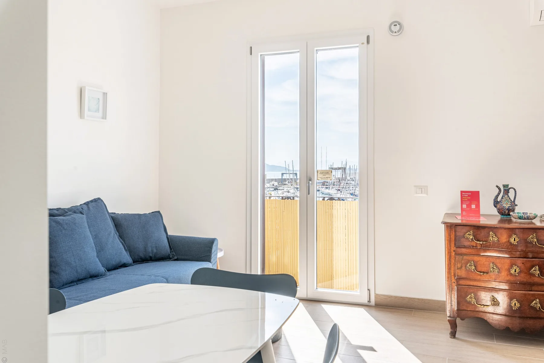 Una sala luminosa con asientos azules junto a puertas de vidrio que dan a un balcón.