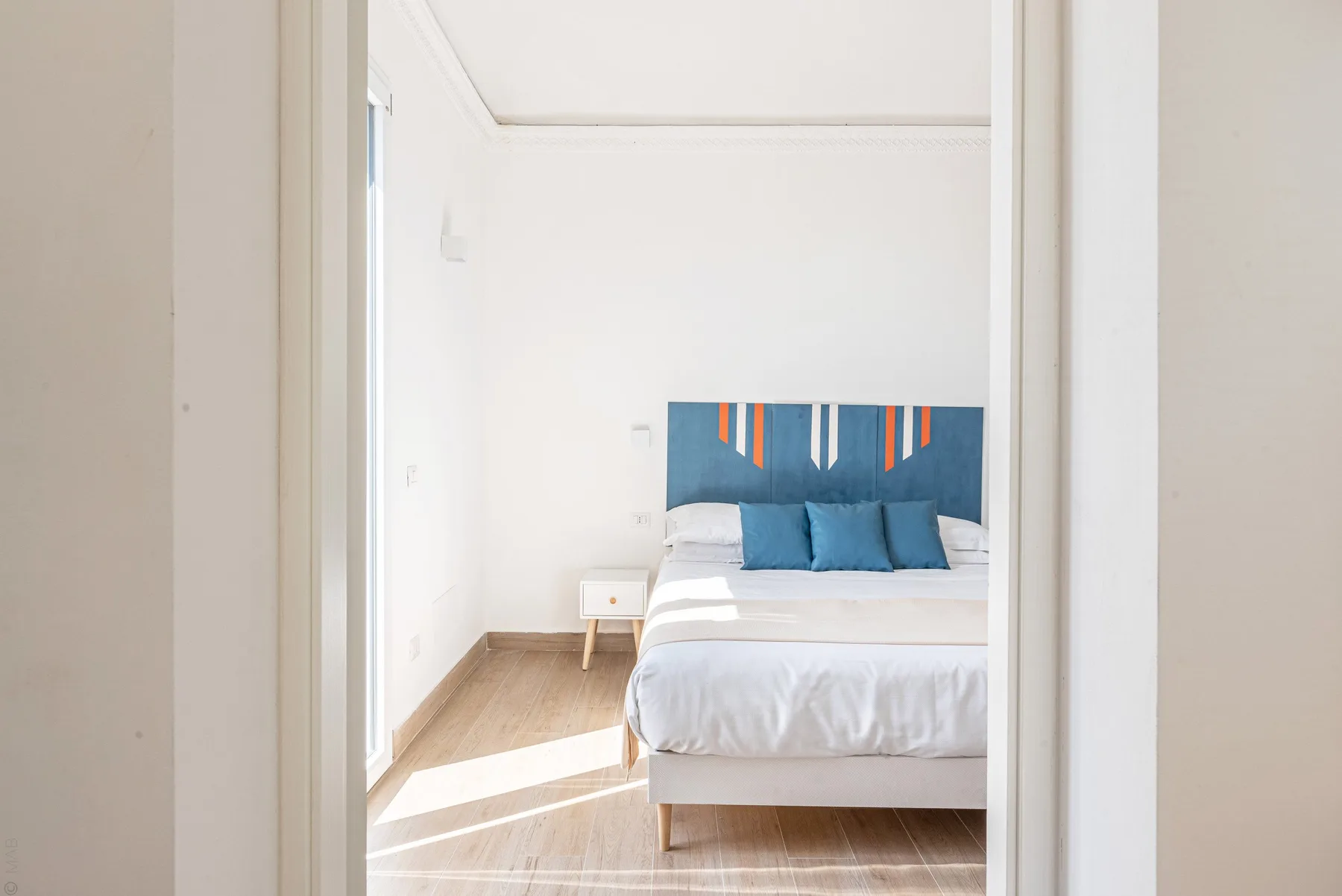 Un dormitorio luminoso con una cama y una obra colorida sobre el cabecero.
