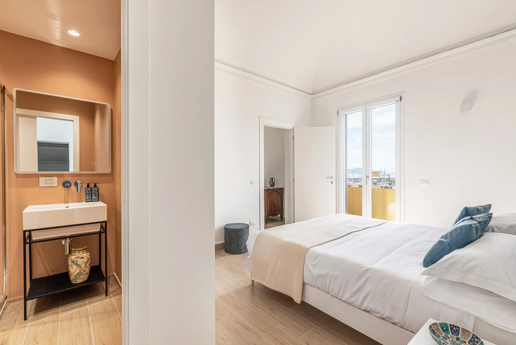 Un dormitorio luminoso con una cama tendida junto a ventanas altas.