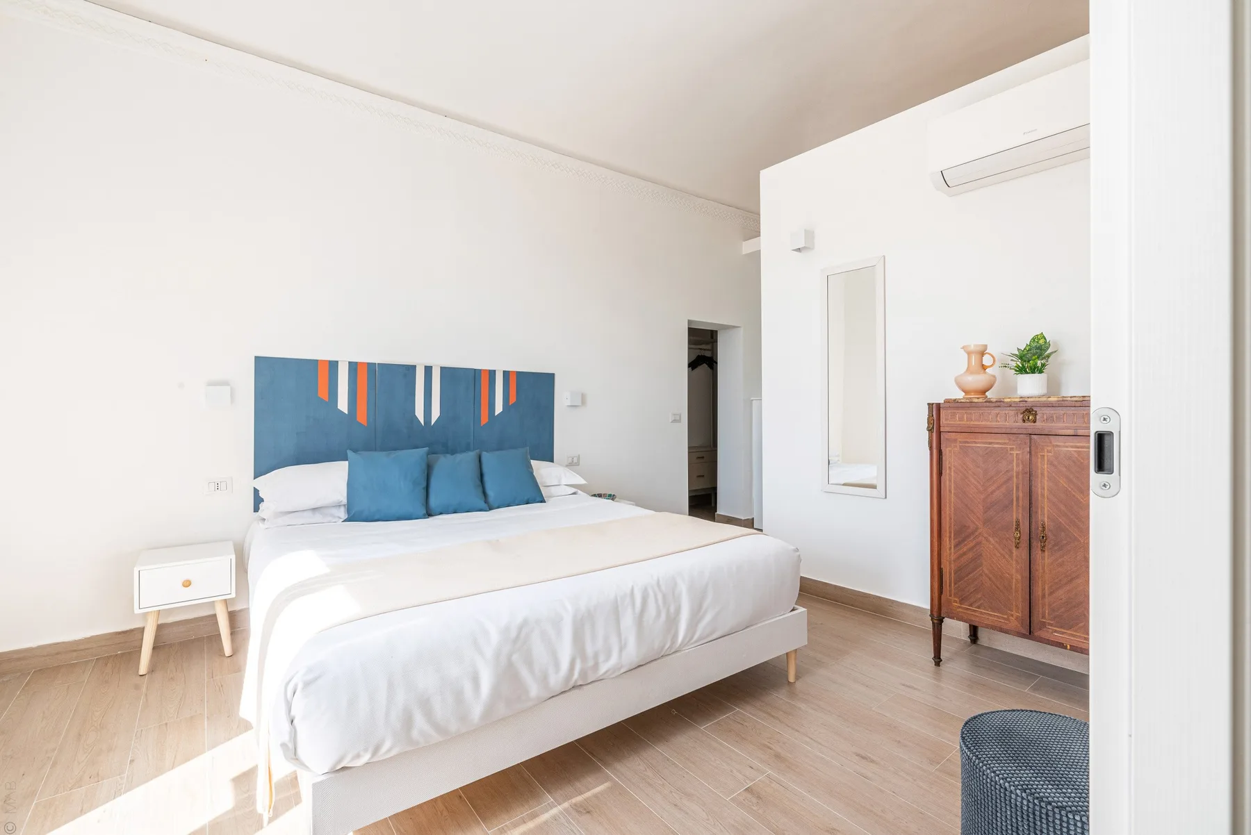 Un dormitorio luminoso con una cama tendida y un armario de madera.
