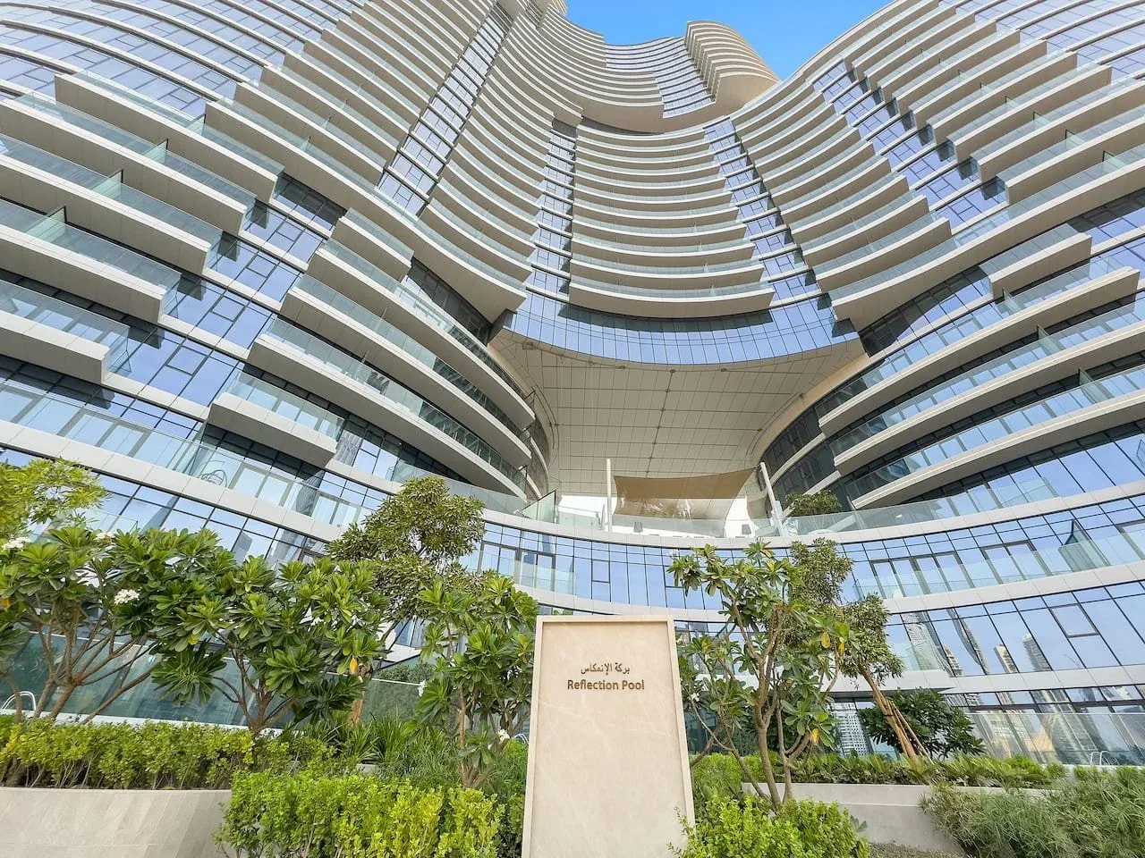Un edificio alto y curvo se eleva sobre jardines y un letrero.