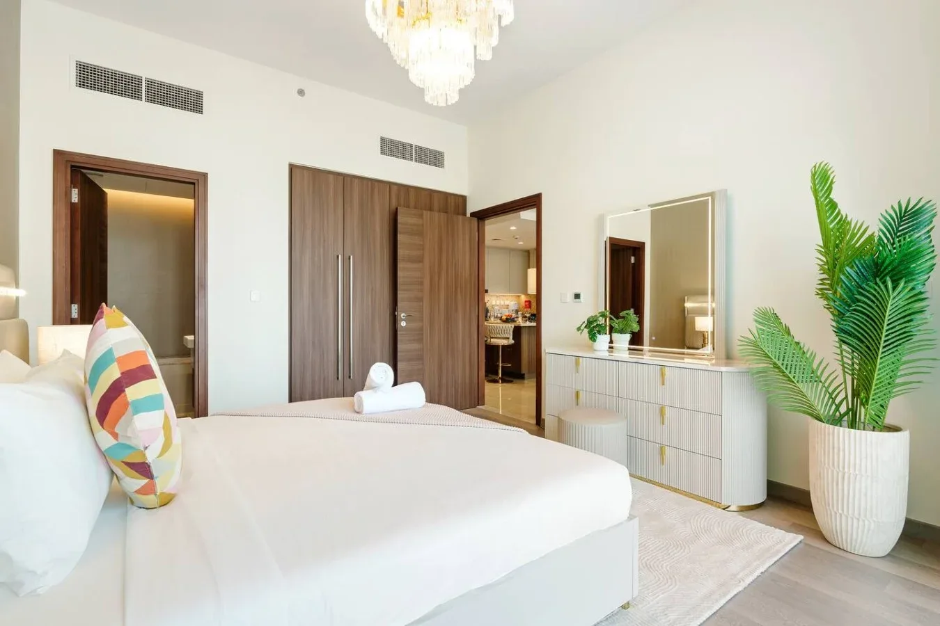 Un dormitorio luminoso con una cama tendida, un armario y una planta en maceta.